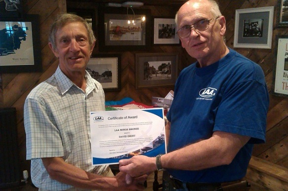 Two elderly men, the one on the right handing a certificate to the one on the left.